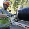 In this 2021 file photo, a worker with the Mason County Public Utility District in Washington state installs a hanger onto fiber-optic cable as it comes off of a spool.