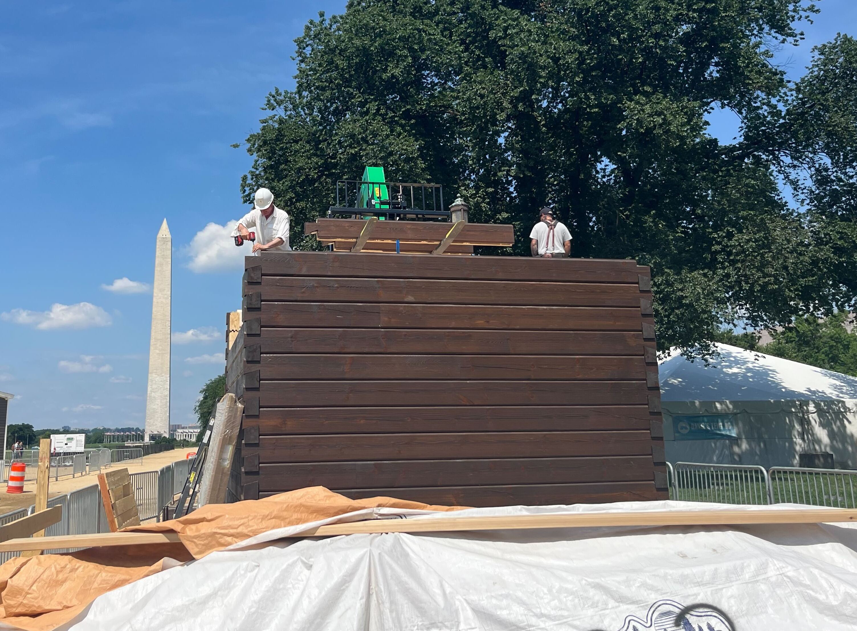 Workers assemble a home resembling an instant log cabin on the National Mall in Washington, D.C., with the Washington Monument behind them. (NPR)