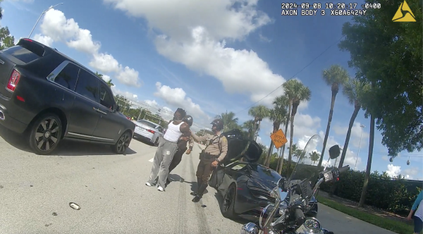 This screenshot from Miami-Dade Police bodycam shows an officer after Dolphins player Tyreek Hill had been handcuffed. Hill is talking to a teammate who has just driven by and witnessed what happened.