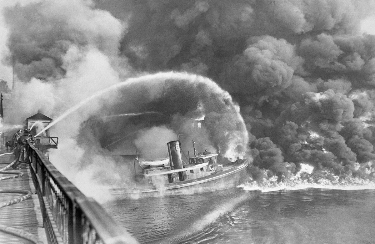 Firefighters stand on a bridge over the Cuyahoga River to spray water on the tug Arizona as a fire, started in an oil slick on the river, engulfs docks in Cleveland on Nov. 1, 1952.