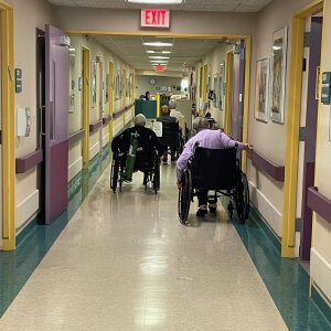 Three people in wheelchairs navigate the hallway of a nursing home. 