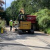 A gas pipeline construction crew in Wyncote, Pennsylvania, replaces older pipes that are prone to leaking climate-heating methane. Men in hard hats work alongside construction equipment on a street that's lined with foliage.