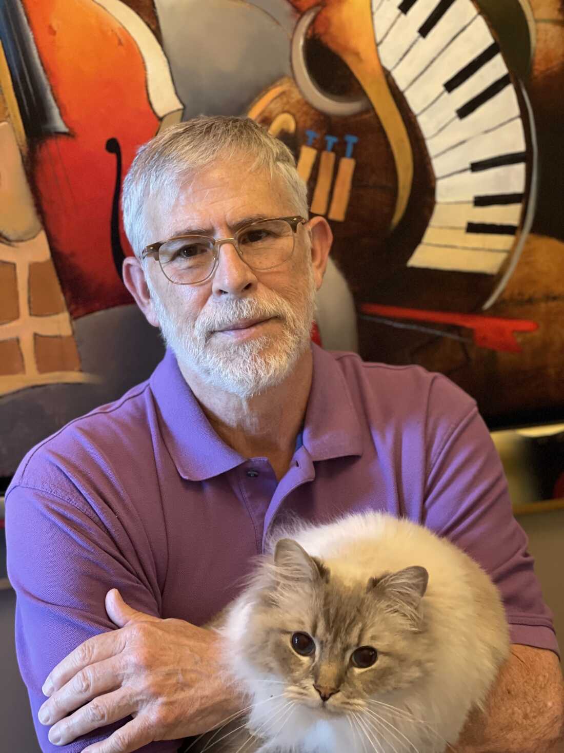 Arnie Beresh is a youthful-looking man in his 70s, pictured here with a fluffy, long-haired gray-white-haired cat. 