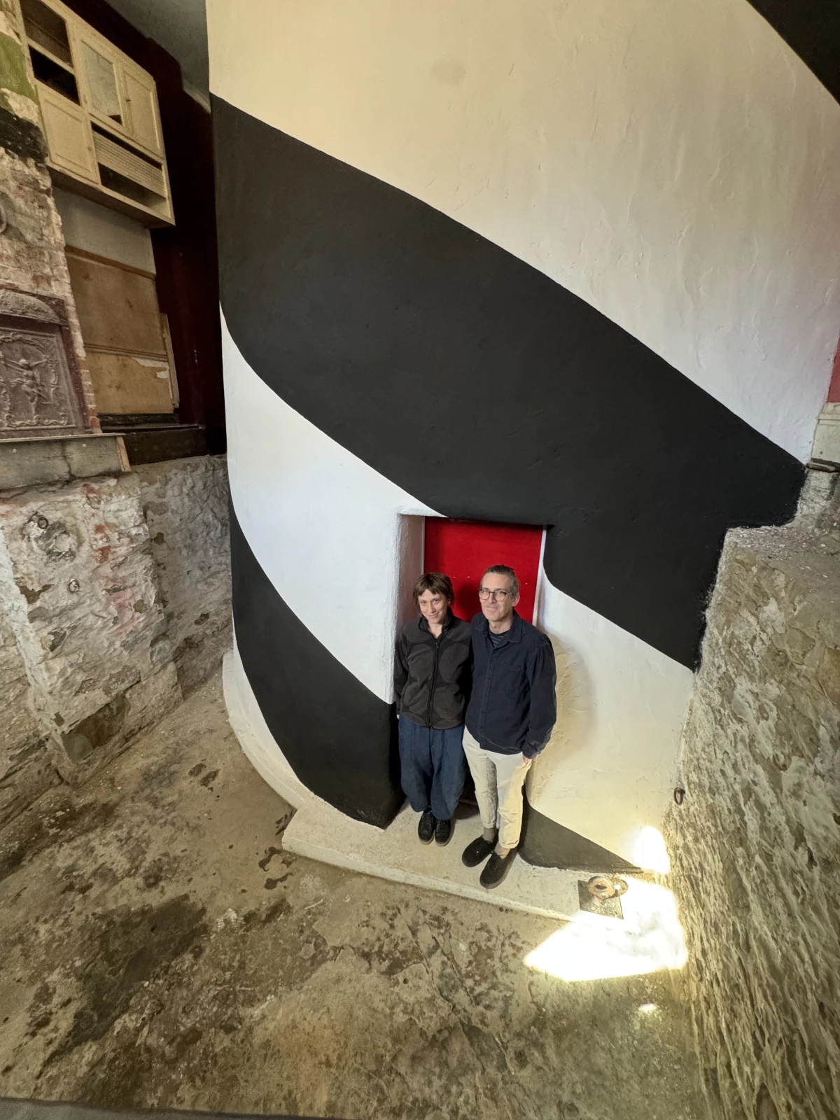 Lenka Clayton and Phillip Andrew Lewis stand next to the base of their working lighthouse, built within a Pittsburgh row house.