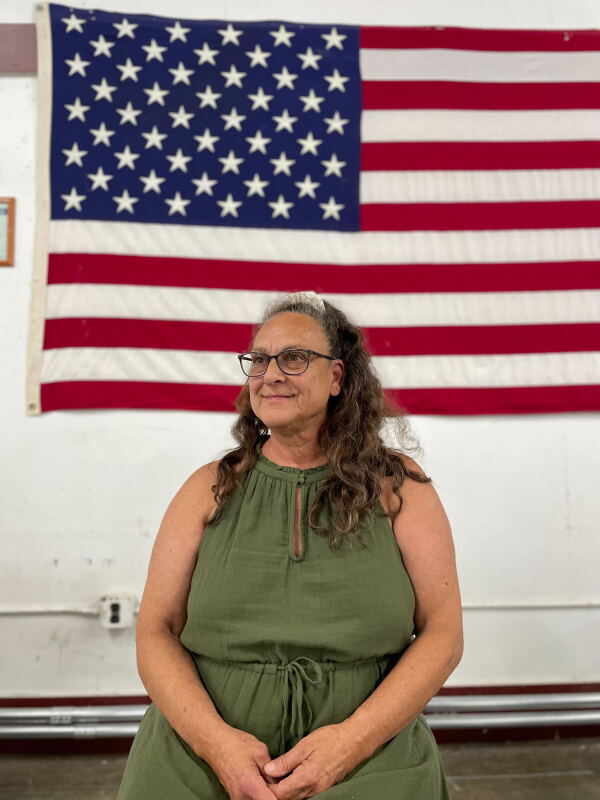 This photo shows Springfield, Ohio, Republican activist Glenda Bailey. She is seated and wearing a green sleeveless dress. An American flag hangs on the wall behind her.