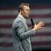 Holding a microphone and wearing a gray suit, Charlie Kirk speaks at Turning Point's Believers' Summit on July 26, 2024, in West Palm Beach, Florida.