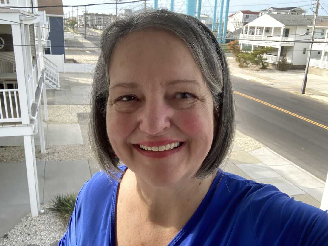 Photographed from about the shoulders up, Pat Gentile smiles for the camera. Behind her is a street lined with houses and buildings.