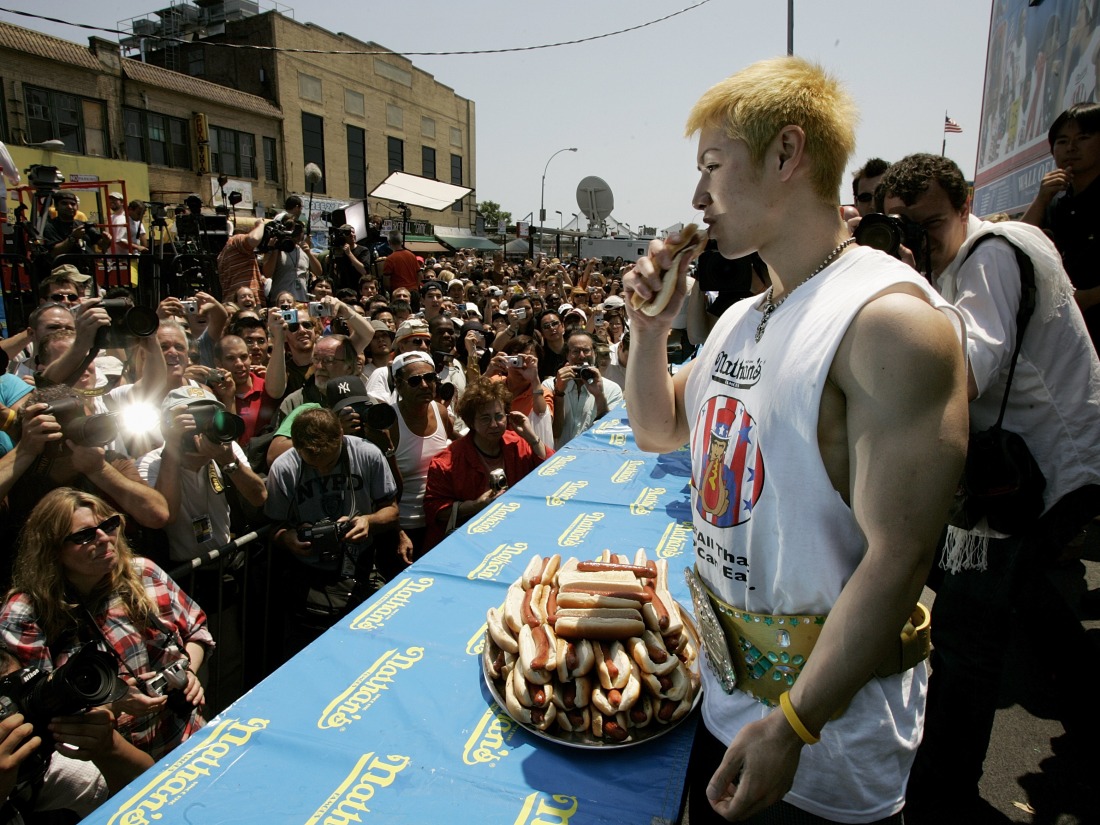 Kobayashi sostiene un hot dog mientras los fotógrafos en una gran multitud toman fotografías.
