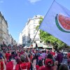 Una bandera blanca con una gran rebanada de sandía está agitado durante la línea roja para el evento Gaza en París el 8 de julio. La mayoría de los manifestantes usan camisas rojas, y caminan en una calle llena de edificios con varios estados.