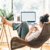 A person sits with their feet up on a desk, scrolling on their phone while their laptop sits open.