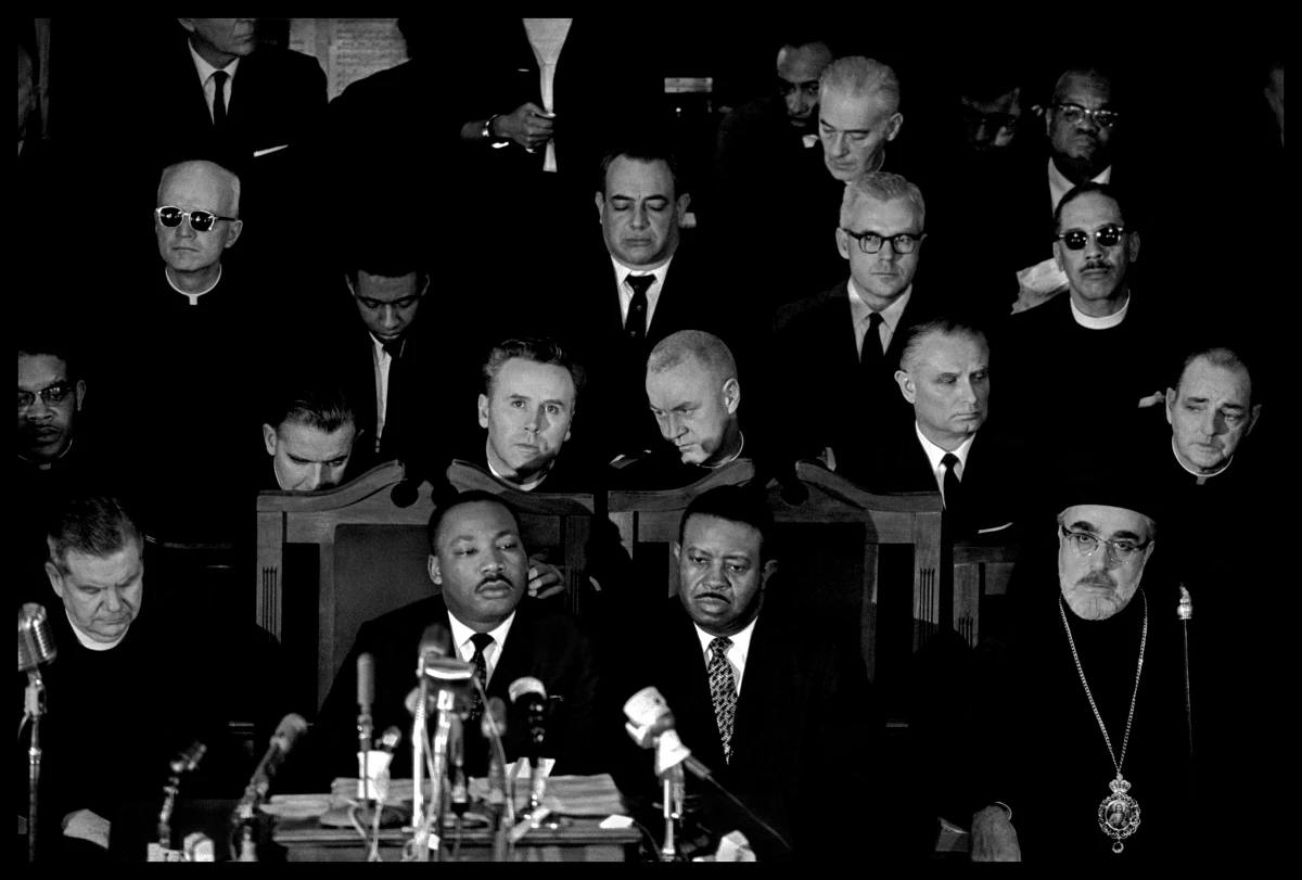 Dr. Martin Luther King, Jr. (center left), Rev. Ralph Abernathy (center right), and Archbishop Iakovos (far right) attend a memorial service for James Reeb. Reeb, a white Unitarian minister from Massachusetts who had answered Dr. King's call for religious leaders to join the protests, was brutally attacked as he left a local Black-owned restaurant on March 9. He died two days later.