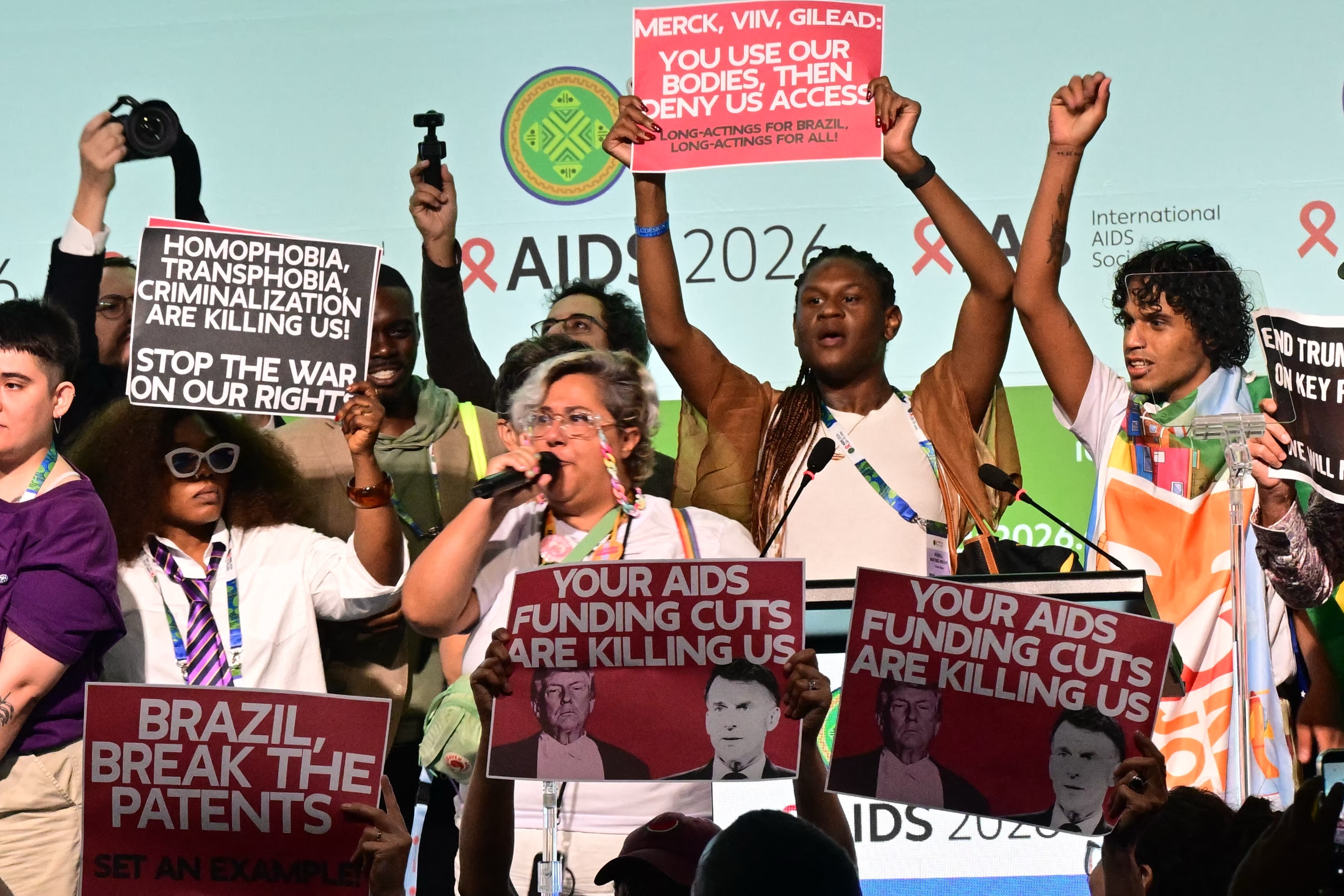 Protesters hold signs, including ones that say "Your AIDS funding cuts are killing us."