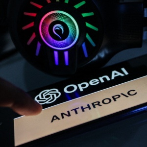 A smartphone displaying the OpenAI logo above the word "Anthropic" is seen beside a lit headset.