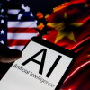 This photo is a close-up view of a smartphone whose screen is displaying "AI" in large letters and the words "Artificial Intelligence" underneath. In the background are the blurred flags of the United States (on the left) and China (on the right).