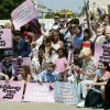 A boisterous crowd of mainly young people fills the photo frame. Printed signs say "Trans kids have always existed" and "Celebrate trans joy," among other slogans.