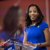 In this 2015 photo, Rep. Mia Love is standing at a lectern with microphones attached to it. She's wearing a blue dress with short sleeves.