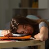 Teenager with long brown hair sleeps on a pile of notebooks.