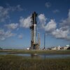 A rocket sits on a launchpad with watery habitat in the foreground.