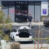 A man walks in a parking lot of a Tesla Collision Center in Las Vegas in front of a building with the word "RESIST" spray-painted on the door.