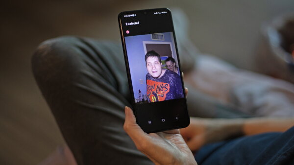 A hand holds a phone showing a photo of a boy wearing a graphic tee. 