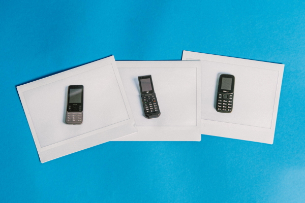 A photograph of three polaroid photos, each showing a different basic phone, the Nokia 6300 4G, the Cat S22 Flip and the BLU Z5 -GSM. The three polaroids are photographed laid out on a bright blue backdrop.