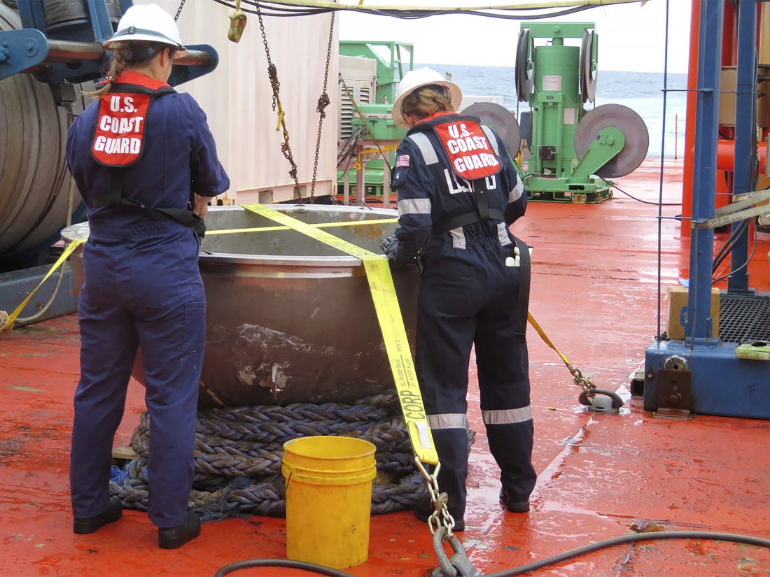 U.S. Coast Guard marine safety engineers inspect the aft titanium endcap from the Titan submersible on a boat.
