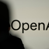 A person in silhouette stands in front of a screen showing OpenAI's logo.