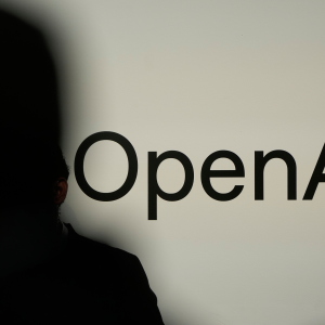 A person in silhouette stands in front of a screen showing OpenAI's logo.
