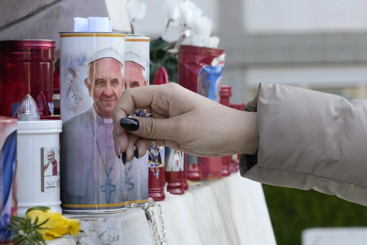 A woman lays a rosary on Saturday near candles adorned with pictures of Pope Francis outside the Agostino Gemelli Polyclinic where Pope Francis is battling pneumonia in Rome.