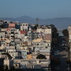 This photo taken at a distance shows houses and buildings in San Francisco's North Beach neighborhood. The structures are mainly various pastel colors such as pink, light blue and butter yellow. Mountains rise in the background.
