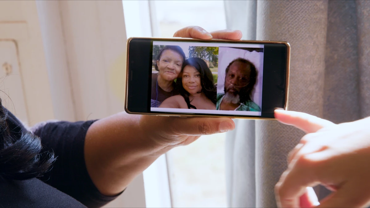 Shalana Jordan holds a photo of her and her parents, Nola and Robert Ramsuer, displayed on her phone.