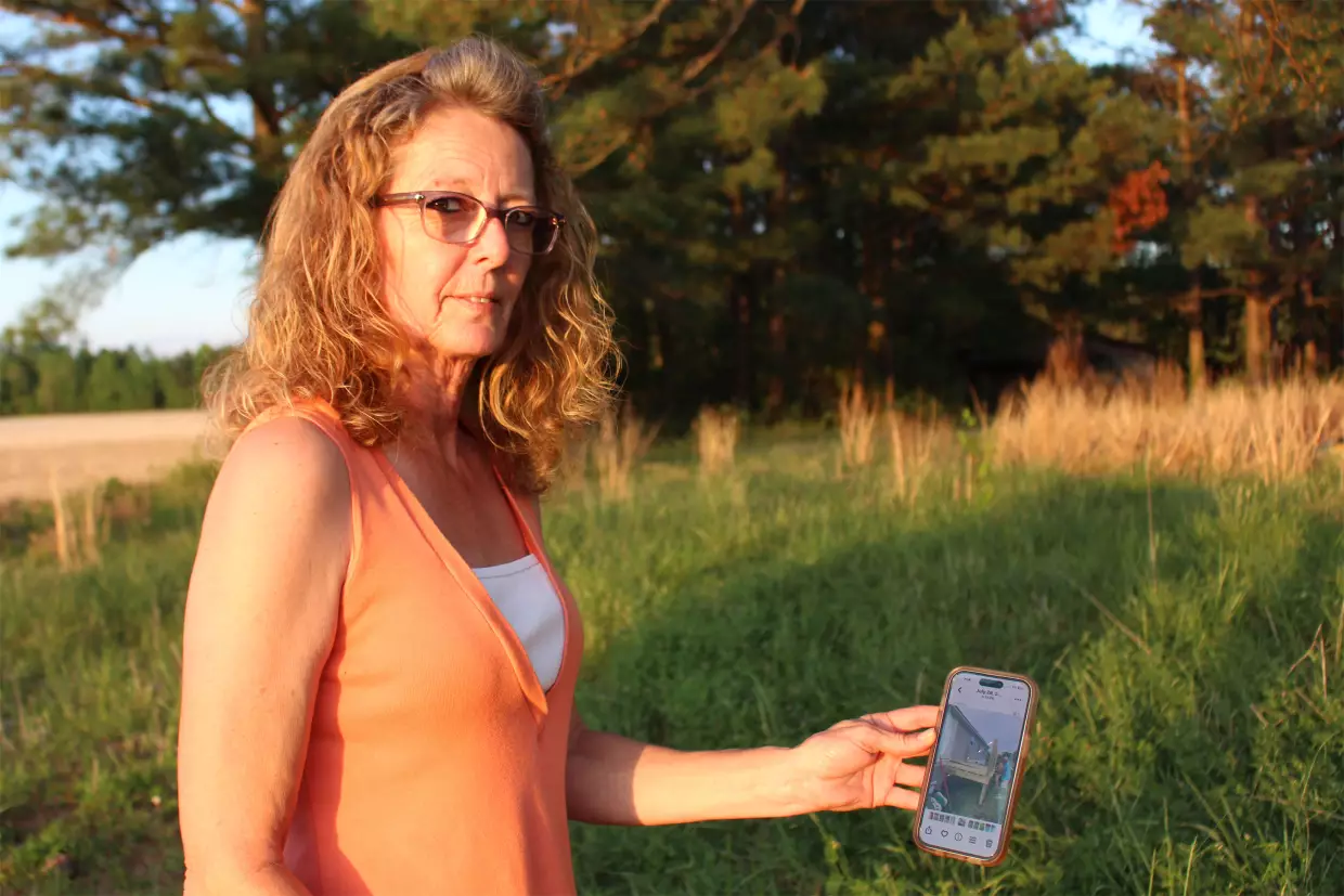 Debra Pierce holds up a picture of Stanley Sears, her brother, while standing in the yard of the mobile home he was renovating before his death in 2024. Pierce believes North Carolina's Martin County needs higher-level emergency services and a hospital.