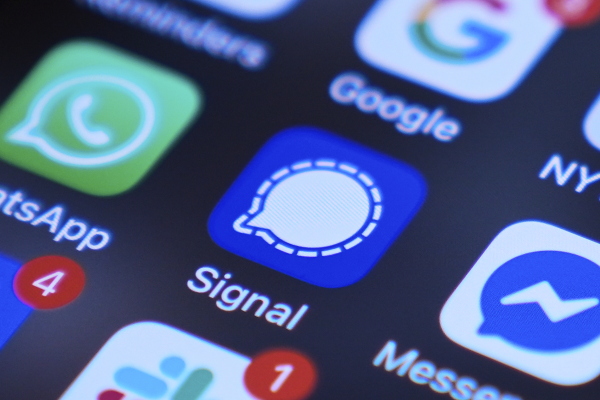 This photo shows a portion of a smartphone's screen, with various app logos arranged in rows. The focus of the photo is the Signal messaging app, whose logo is a white comment bubble against a blue background.