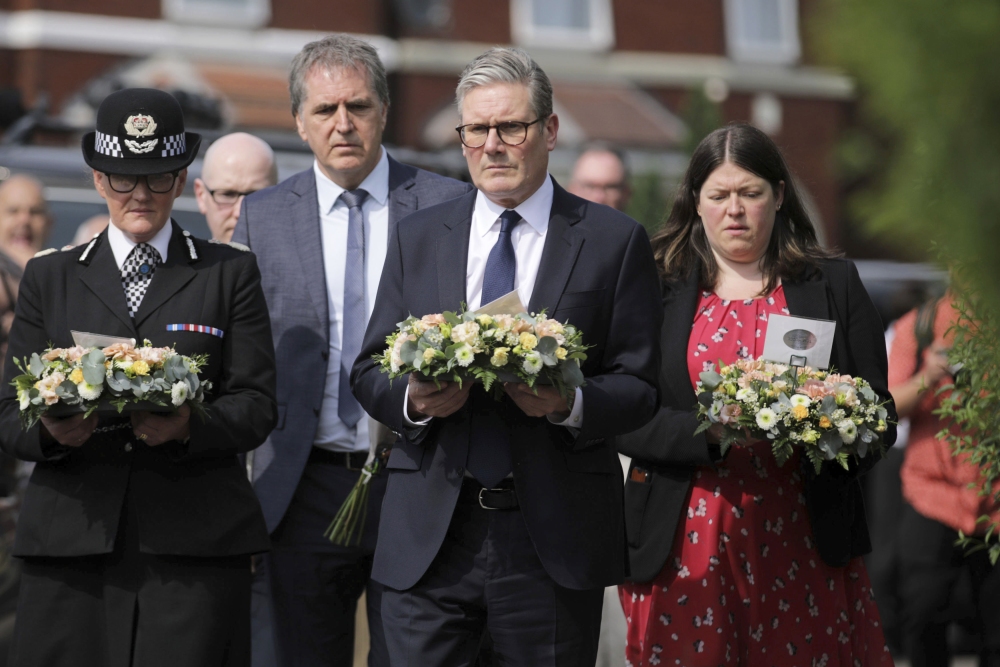 British Prime Minister Keir Starmer (center) carries a floral tribute on Tuesday near the scene of a deadly knife attack at a dance school a day earlier in Southport, England. (PA via AP)
