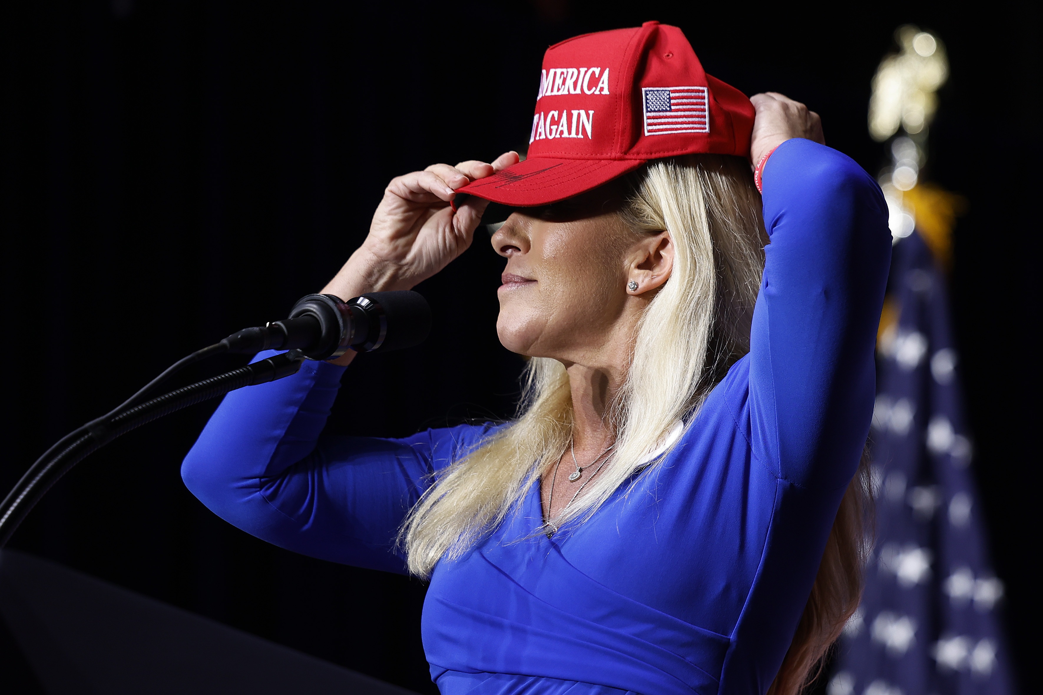 Then-Rep. Marjorie Taylor Greene puts on her red "Make America Great Again" baseball cap while addressing a campaign rally for then-candidate Donald Trump in March 2024 in Rome, Georgia.