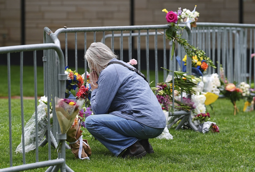 A visitor offers a tribute after leaving a bouquet of flowers at a makeshift memorial for victims of an attack outside of the Boulder County, Colo., courthouse as a light rain falls Tuesday, June 3, 2025, in Boulder, Colo. (AP Photo/David Zalubowski)