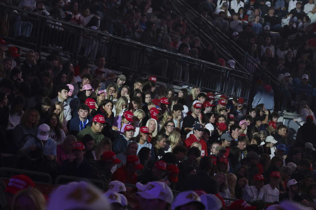 People sit in the rows of an arena as they attend a Turning Point USA event at the University of Mississippi on October 29, 2025. Many people are wearing red Make America Great Again baseball caps.