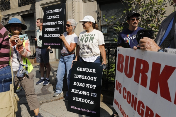 Protesters hold sigs that say, "Children cannot consent to puberty blockers" and "Gender ideology does not belong in schools."