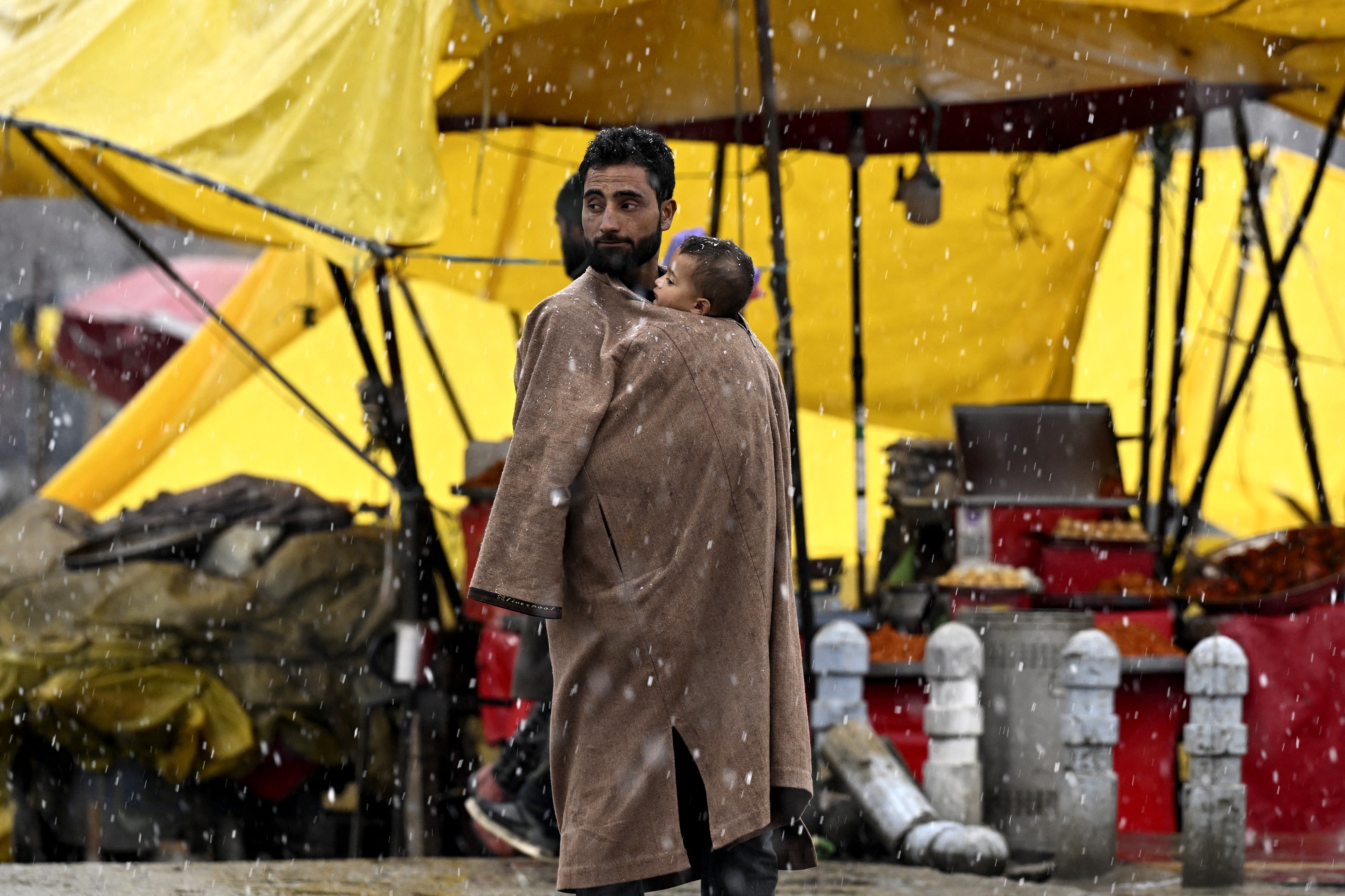 A man carries a child in his Kashmiri <em>pheran,</em> a traditional winter coat that gives warmth during the coldest days of winter. A pot of embers carried beneath the fabric adds to the comfort.