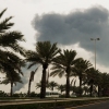 A plume of smoke rises into the sky after a reported Iranian strike on fuel tanks in Muharraq, Bahrain, on March 12. On the ground is a road lined with palm trees.