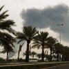 A plume of smoke rises into the sky after a reported Iranian strike on fuel tanks in Muharraq, Bahrain, on March 12. On the ground is a road lined with palm trees.