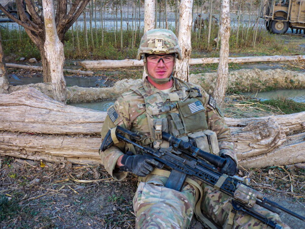 Dustin Ingram is photographed in uniform holding a large rifle in while sitting on the ground in eastern Afghanistan.