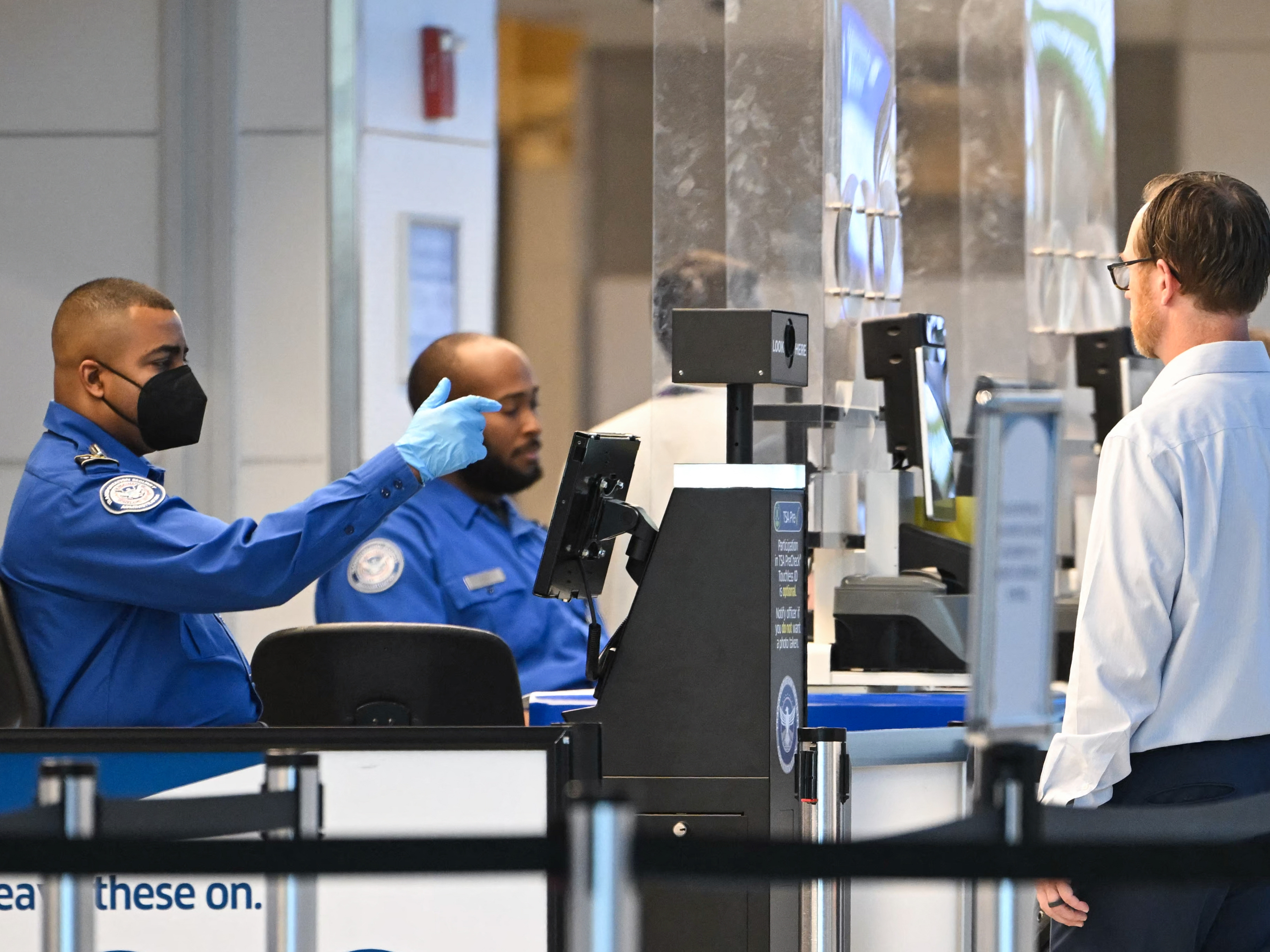 TSA agents check passenger identity documents at a security checkpoint at Reagan National Airport on the first day of the government shutdown in Arlington, Va., on Oct. 1. Some airports are declining to play a video where Homeland Security Secretary Kristi Noem blames Democrats for the government shutdown.