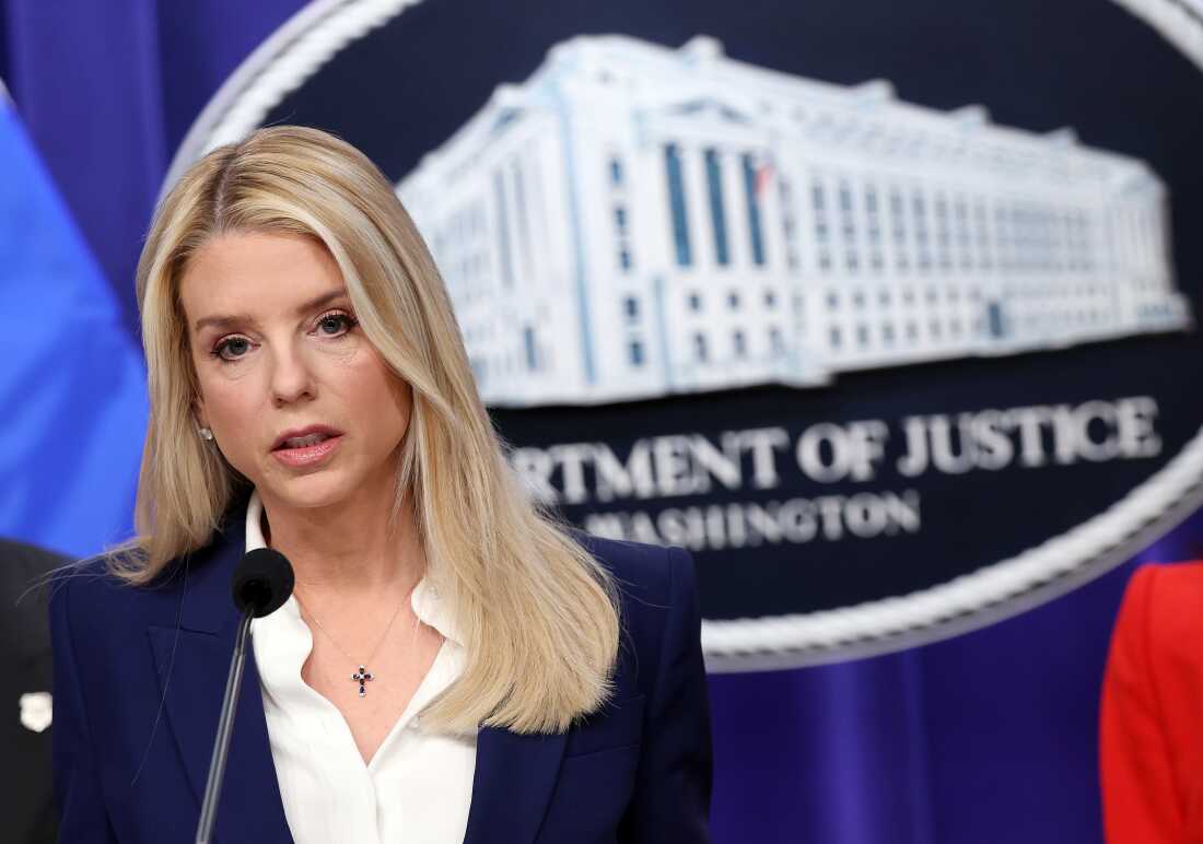Attorney General Pam Bondi stands in front of a Department of Justice sign to deliver remarks.