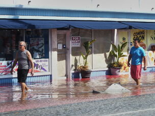 Pedestrians walk through a flooded street caused by king tides and heavy rain Wednesday, Oct. 28, 2026, in North Bay Village, Fla.