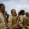 Female Marine Corps recruits from Lima Company stand as they receive a safety briefing. They are wearing uniforms with a pixelated camouflage pattern.