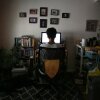 A woman is shown from behind at a sitting at a desk facing a computer screen. An array of small, framed photographs are on the wall above the computer.