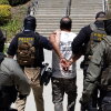 Four Immigration and Customs Enforcement agents walk a detainee out of the Ventura County Government Center in Ventura, California, on July 27. The individuals are photographed with their backs to the camera, and the detainee is handcuffed behind his back. The agents are wearing bulletproof vests that say