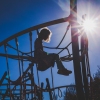 Little girl with curly hair sits on top of a playground jungle gym.
