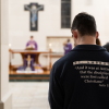 Students of St. Ambrose University, photographed from behind, attend Mass. A crucifix is on the wall in the background.